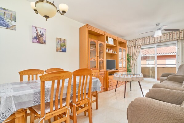 A dining area with wooden chairs and a table, a cabinet with glass doors, a television, and a ceiling fan.