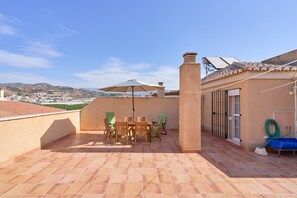 Eine Dachterrasse mit Tisch und Stühlen, einem großen Sonnenschirm und einem Schlauch.