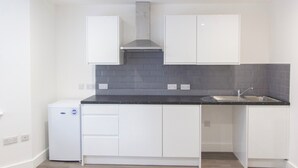 Cocina compacta con armarios blancos, encimera negra y extractor de acero inoxidable.