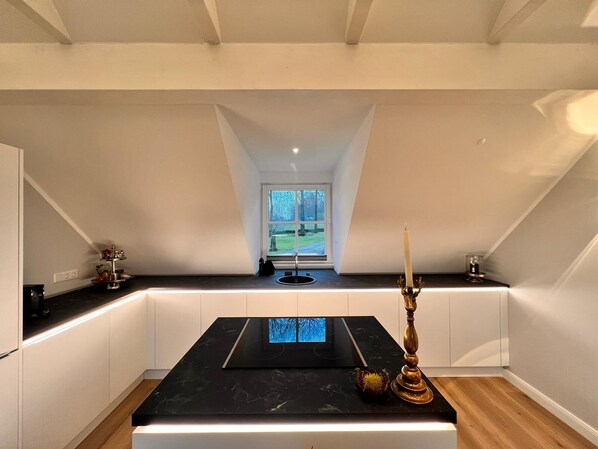 A modern kitchen with a black countertop, a built-in stove, and a window with a view of a green landscape. - LandGut & Residenz Driehof (Tecklenburg)