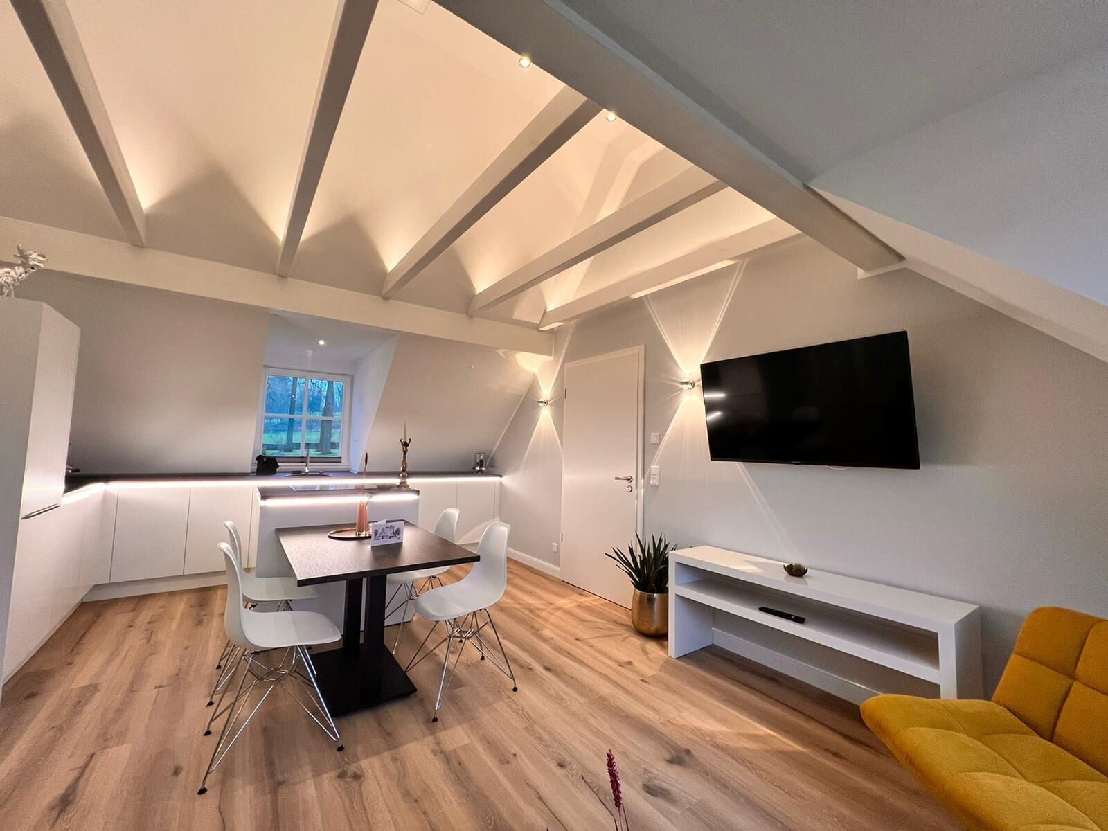 Um apartamento moderno do tipo loft, com área de jantar, cozinha e sala de estar, apresentando teto inclinado e televisão de tela plana na parede.