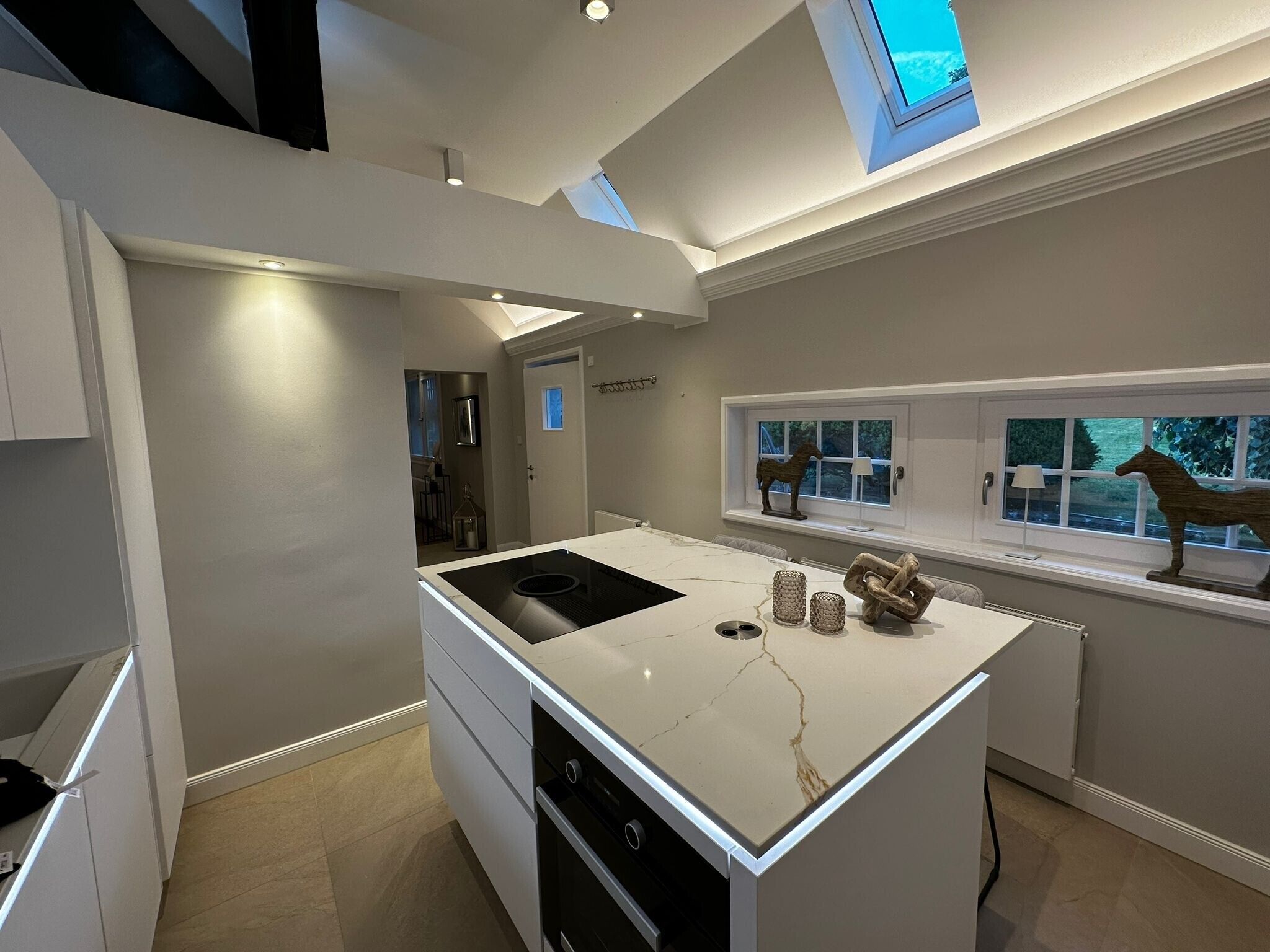 A modern kitchen with a central island, a skylight, and a window with decorative horses.