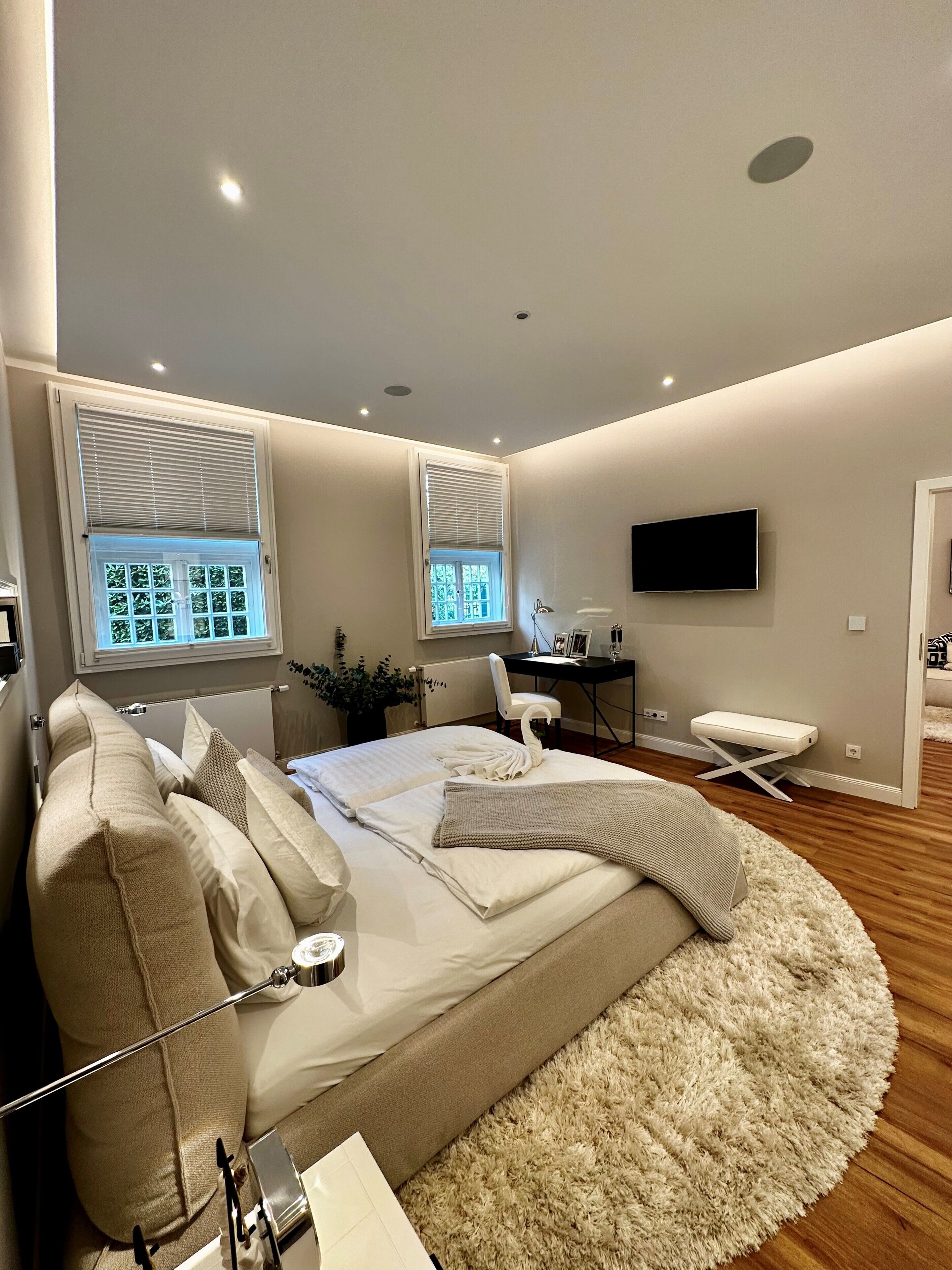 A modern bedroom with a bed, bedside tables, a desk, a chair, and a TV.