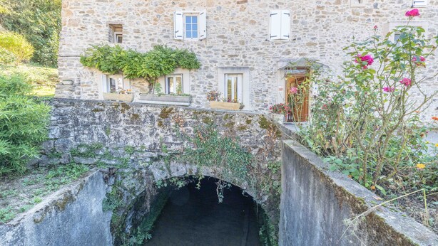 Un bâtiment en pierre doté d’une entrée en forme de tunnel, de fenêtres avec volets et de plantes en pot.