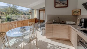 Une cuisine moderne avec une table à manger en verre, des meubles de rangement en bois et une vue sur l’extérieur.