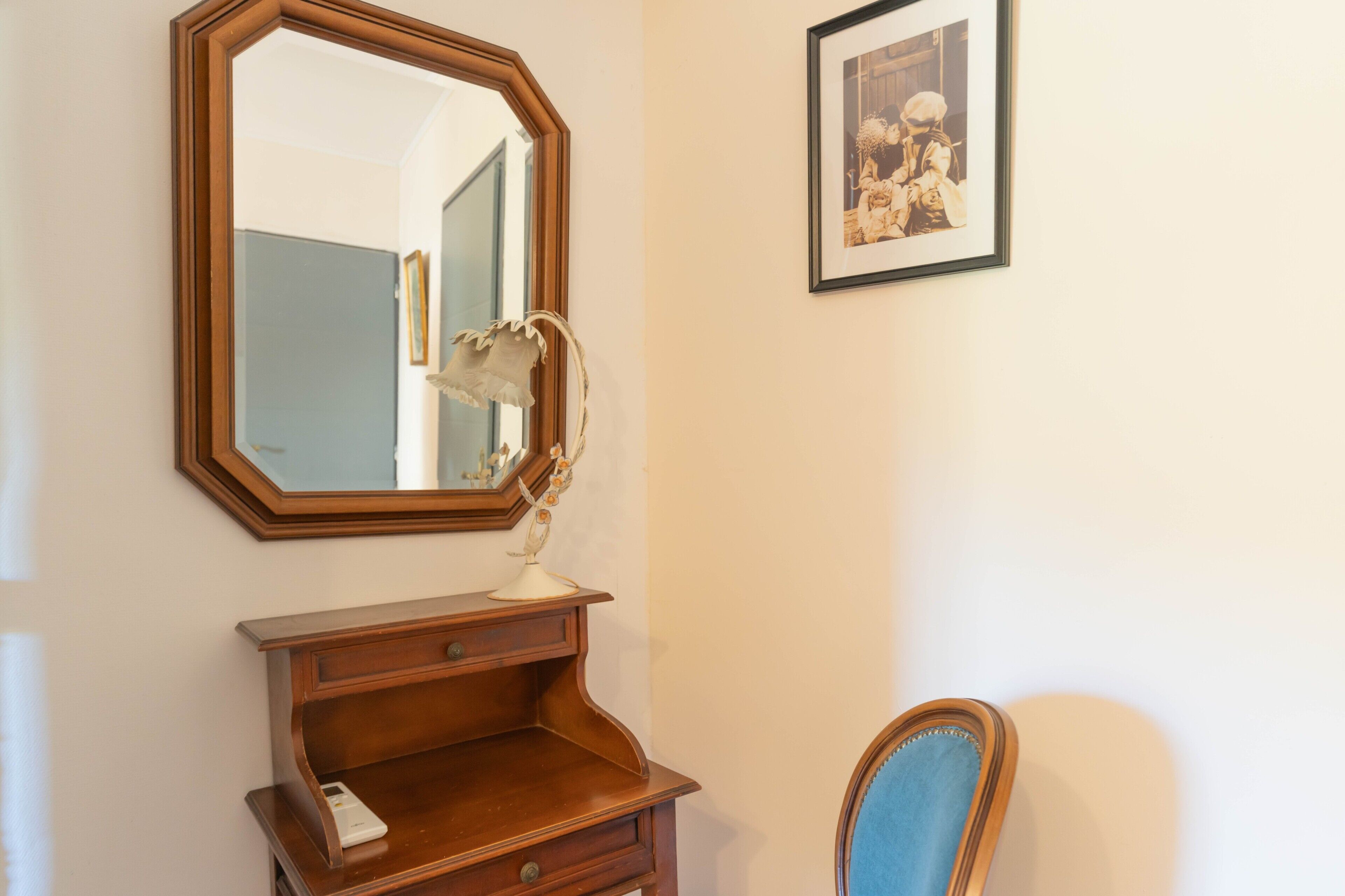 A room with a wooden dresser, a mirror, a framed picture, and a blue chair.