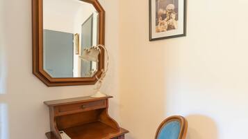A room with a wooden dresser, a mirror, a framed picture, and a blue chair.
