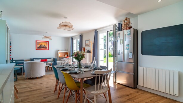 A modern kitchen with a dining area, wooden flooring, and large windows.