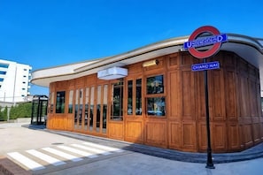 A building with a curved wooden facade, a clear blue sky, and a street sign indicating 'UHRICSCHEID D' and 'CHIANG MAI'. - Springday House Pool Villa Near Nimman (Chiang Mai)