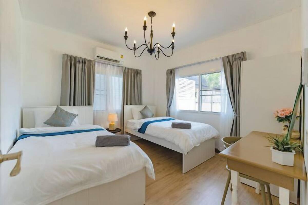 Une chambre d’hôtel avec deux lits simples, une table en bois, un lustre et une fenêtre avec des rideaux.