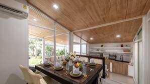 A modern kitchen with a wooden ceiling, a dining area with a long table set for four, and a view of the outdoors. - Springday House Pool Villa Near Nimman (Chiang Mai)