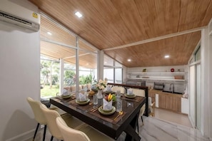 A modern kitchen with a wooden ceiling, a dining area with a long table set for four, and a view of the outdoors. - Springday House Pool Villa Near Nimman (Chiang Mai)