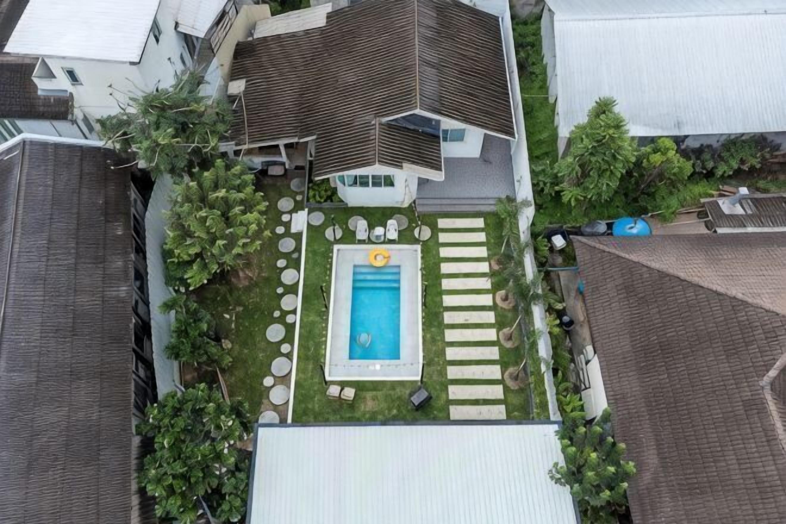 An aerial view of a residential backyard with a swimming pool, a lawn, and a patio area.