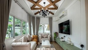 A living room with a sofa, ottoman, coffee table, and a TV mounted on the wall. - Springday House Pool Villa Near Nimman (Chiang Mai)