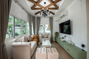 Ein Wohnzimmer mit Sofa, Hocker, Couchtisch und einem an der Wand befestigten Fernseher.