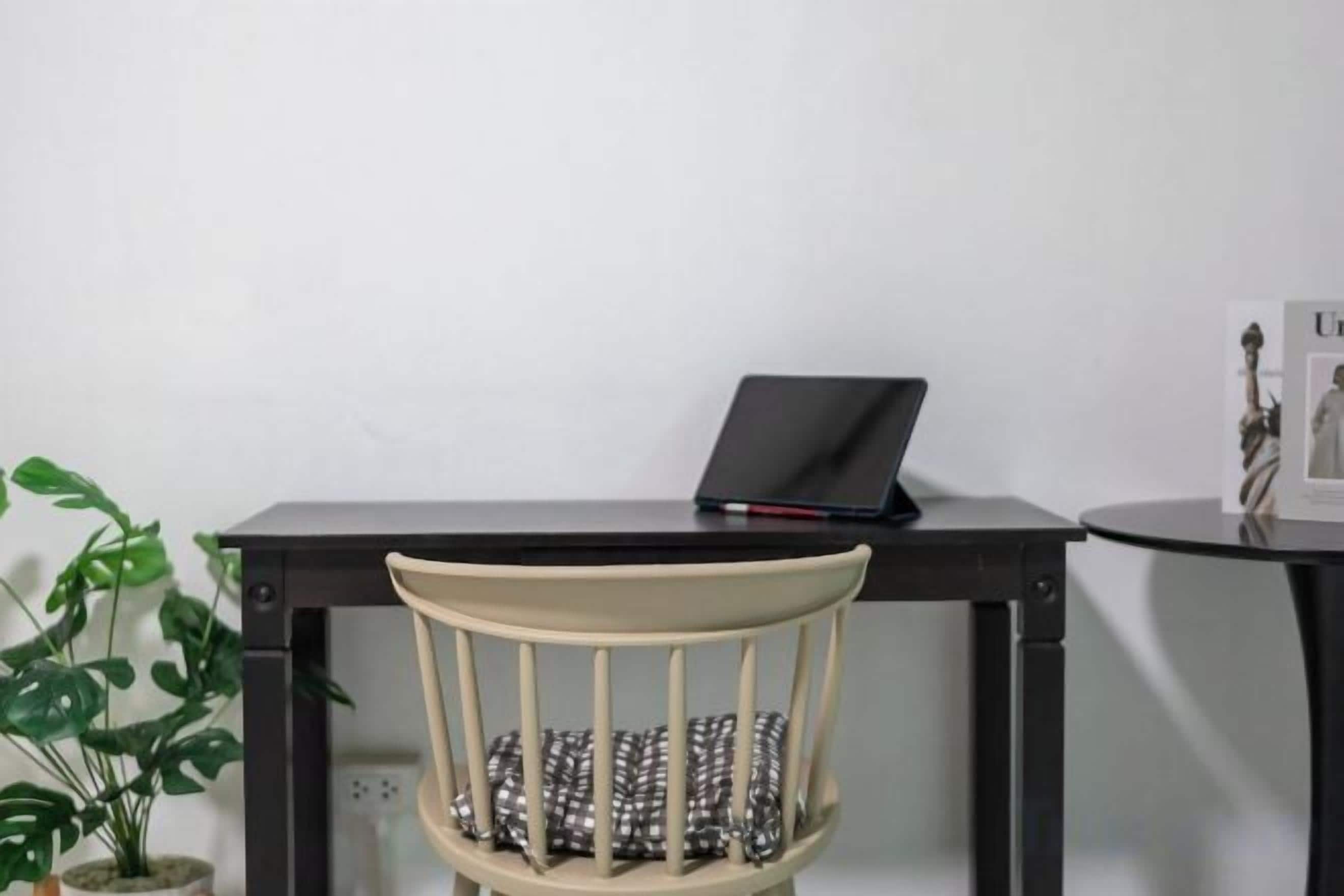 Une chaise avec un coussin, un ordinateur portable sur un bureau et une petite table sur laquelle se trouve une statue.