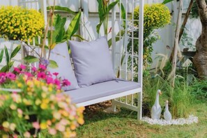 A garden with a white swing chair, surrounded by various plants and flowers. - Springday House Pool Villa Near Nimman (Chiang Mai)