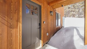 A wooden exterior with a gray door, a window, and a snow-covered ground. - Family-Friendly Cabin Escape (Idaho Springs)