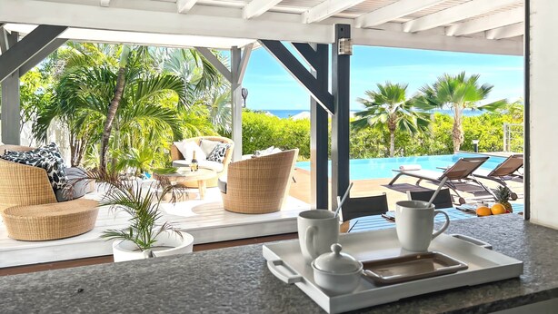 Un espace extérieur aménagé avec des meubles en osier, une piscine et une vue sur l’océan.