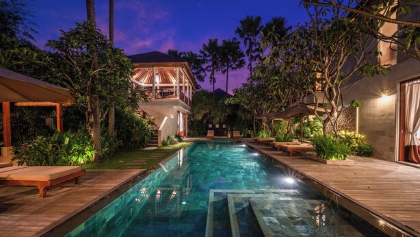 A swimming pool with a wooden deck, surrounded by lush greenery and palm trees, leading to a building with a balcony. - The Complete Guide to Renting Your Exclusive Holiday Villa in Kabupaten Badung with Private Pool and Fully Staffed (Bali)