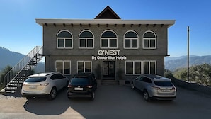 Un edificio con el letrero 'Q'NEST By Quadrillion Hotels' y tres coches estacionados frente a él.