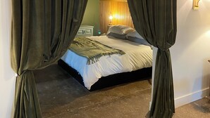 A bedroom with a bed, curtains, a wall-mounted lamp, and a textured wall.