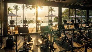 Uma academia com equipamentos de ginástica e vista para o oceano ao pôr do sol.