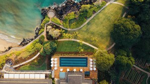 Vista aérea de uma propriedade costeira com piscina, jardim e caminho para a praia.