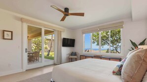 A bedroom with a large bed, a ceiling fan, a TV, and a view of the outdoors. - Wai'ula'ula J101 Three Bedroom (Kamuela)