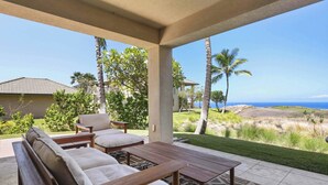 A covered patio with a wooden bench and table, overlooking a grassy area with palm trees and a view of the ocean. - Wai'ula'ula J101 Three Bedroom (Kamuela)