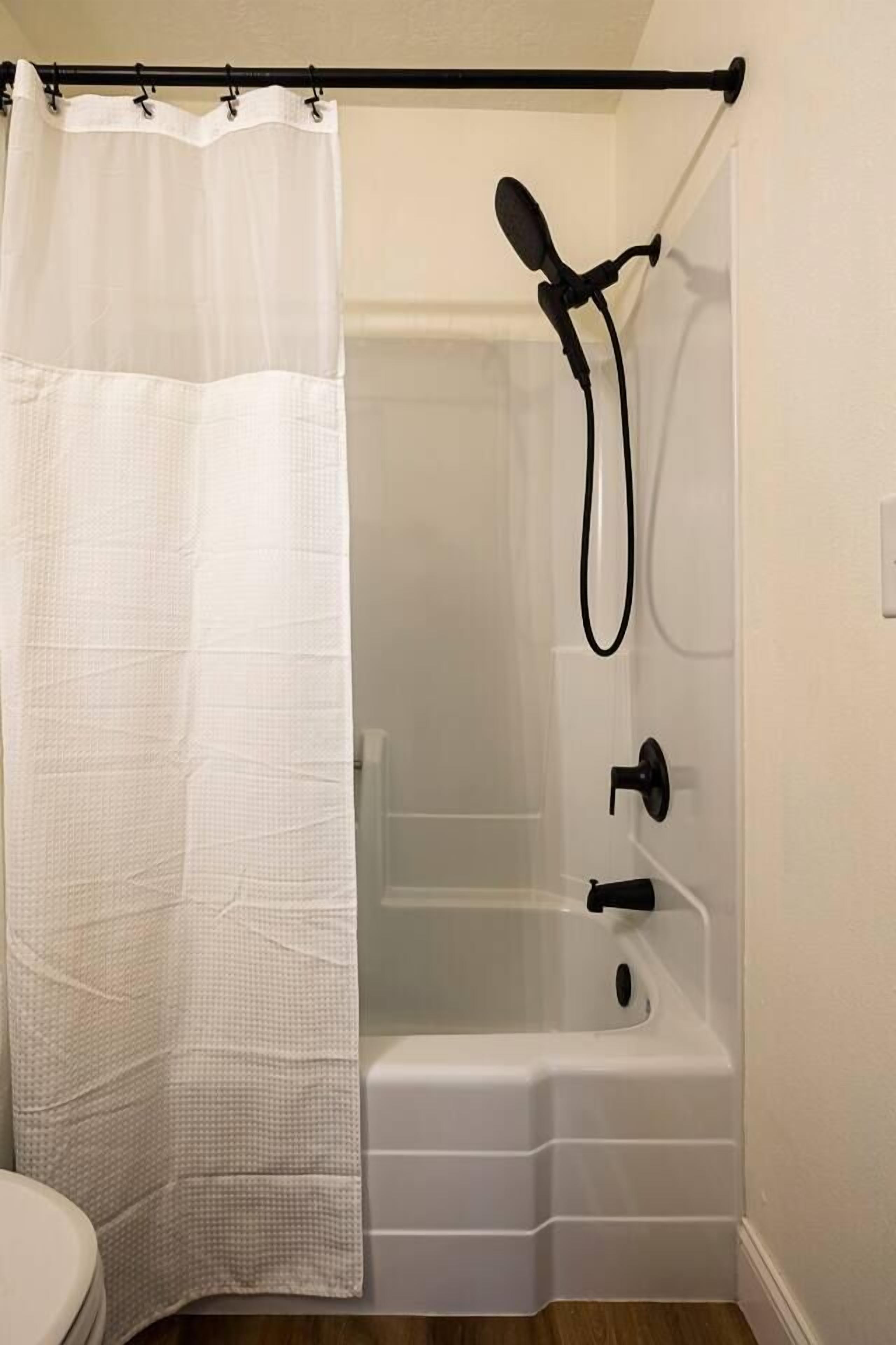 A bathroom with a shower, a white bathtub, and a white toilet.
