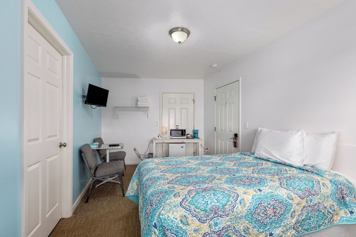 A bedroom with a bed, a desk with a computer, a chair, and a TV mounted on the wall.