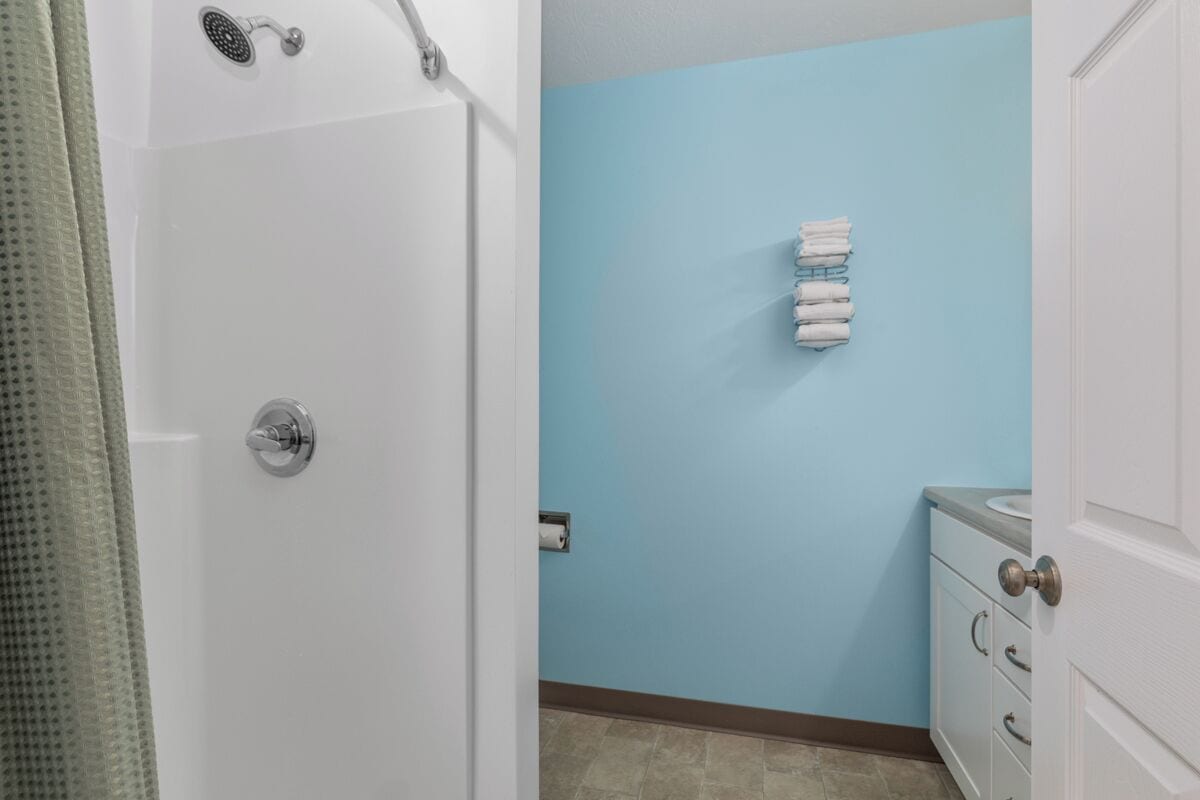 A bathroom with a white door, a blue wall, a towel rack with towels, and a white cabinet with drawers.