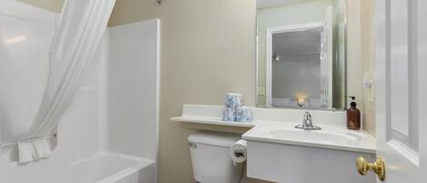A bathroom with a bathtub, toilet, sink, and vanity mirror with lights.