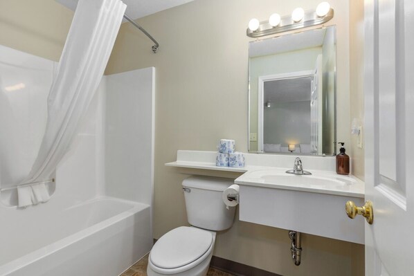 Une salle de bain équipée d’une baignoire, de toilettes, d’un lavabo et d’un miroir avec éclairage intégré.
