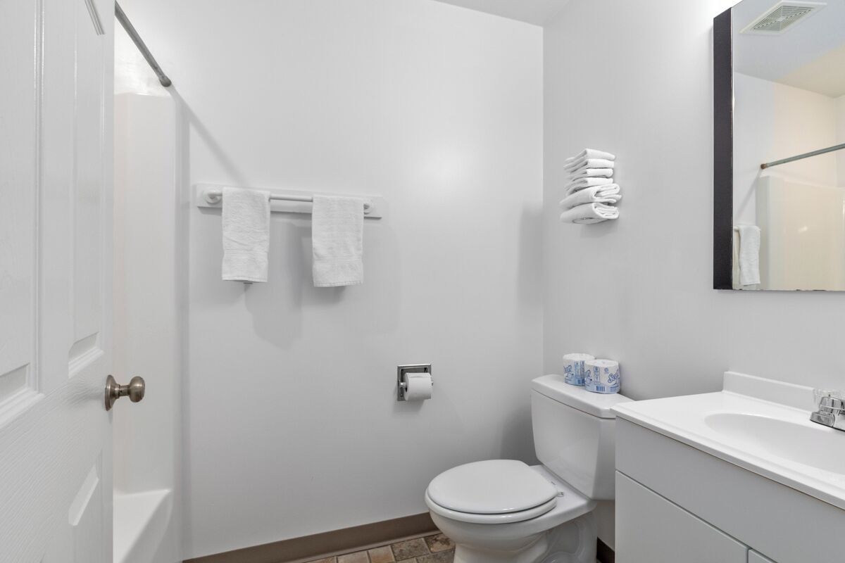 A bathroom with a white toilet, a sink, and a mirror. There are towels hanging on a rack and a roll of toilet paper on the wall.