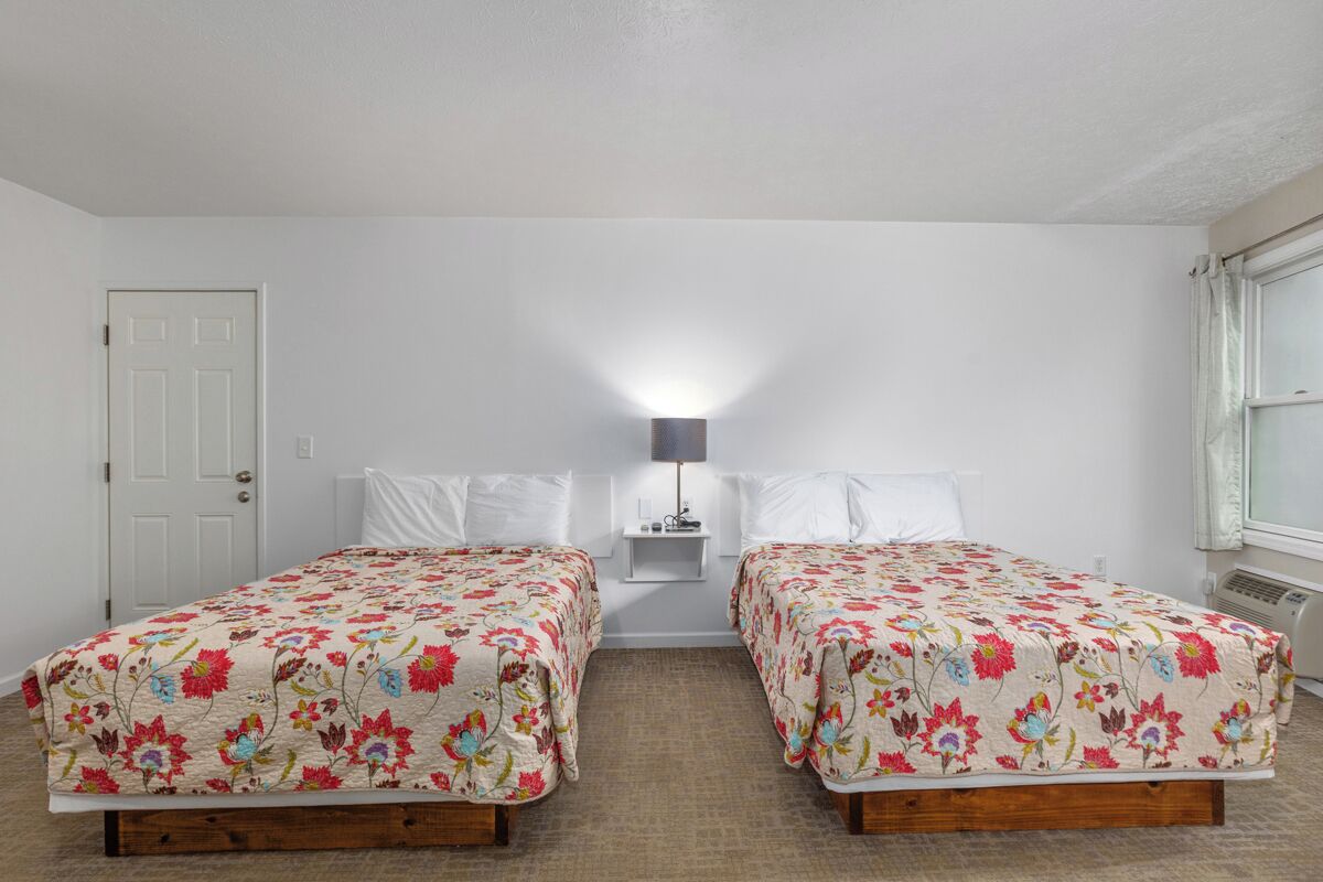 Ein Zimmer mit zwei Betten, einem Nachttisch, einer Lampe, einer Tür und einem Fenster.