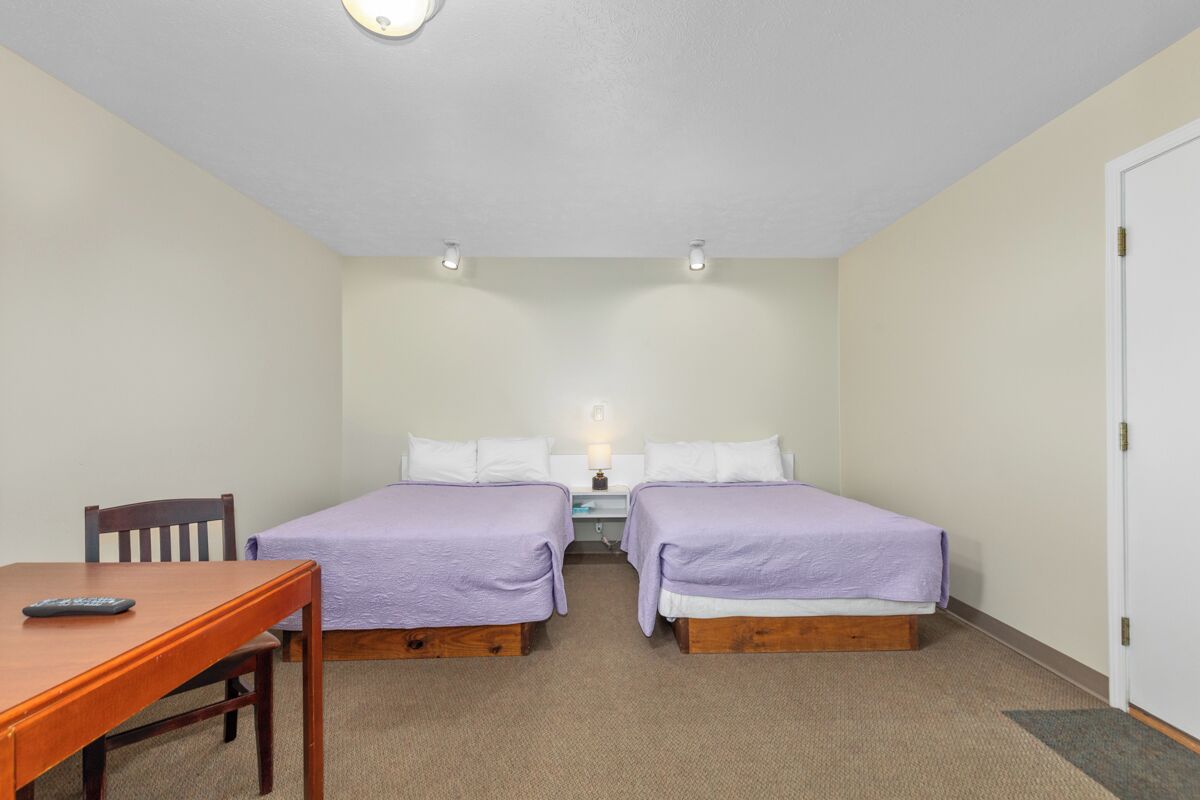 Ein kleines, sauberes Zimmer mit zwei Einzelbetten, einem Holztisch und einem Schreibtisch mit Stuhl.