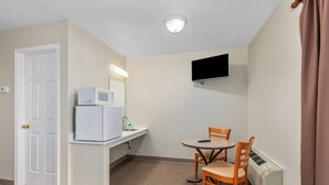 A compact room with a kitchenette, a dining table with chairs, a flat-screen TV mounted on the wall, and a door. - The Lakeview Motel (Lake City)