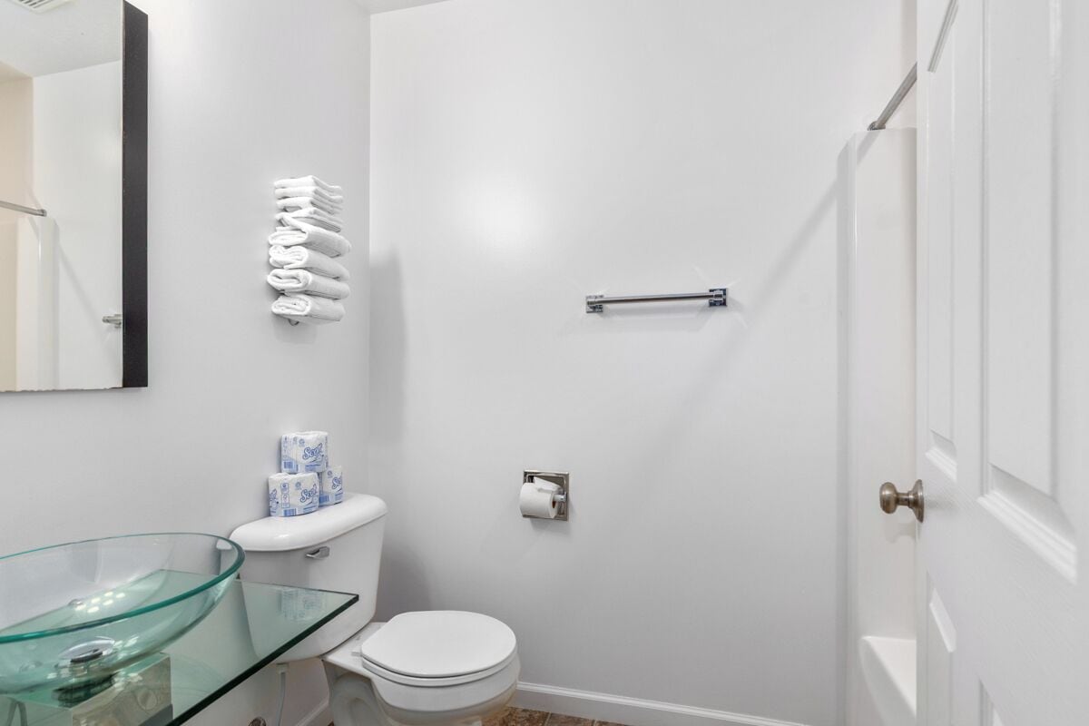 A bathroom with a glass vessel sink, white toilet, and a towel rack.