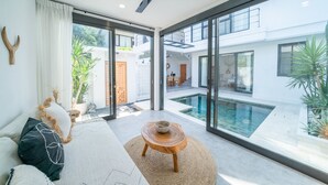 A modern living room with a large glass door leading to a pool area, a ceiling fan, and a view of a two-story building.