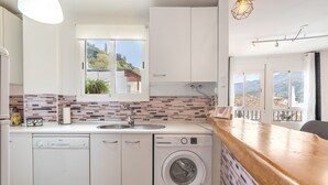 Une cuisine moderne équipée d’un lave-vaisselle, d’un lave-linge et d’une grande fenêtre donnant sur l’extérieur.