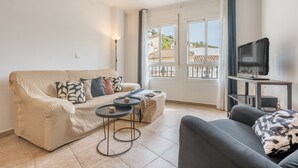 Un salon comprenant un canapé, un petit divan, un téléviseur posé sur un meuble et un balcon avec vue.