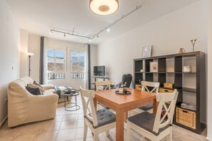 Ein modernes Wohnzimmer mit einer Couch, einem Esstisch, Stühlen, einem Fernseher und einem Bücherregal.