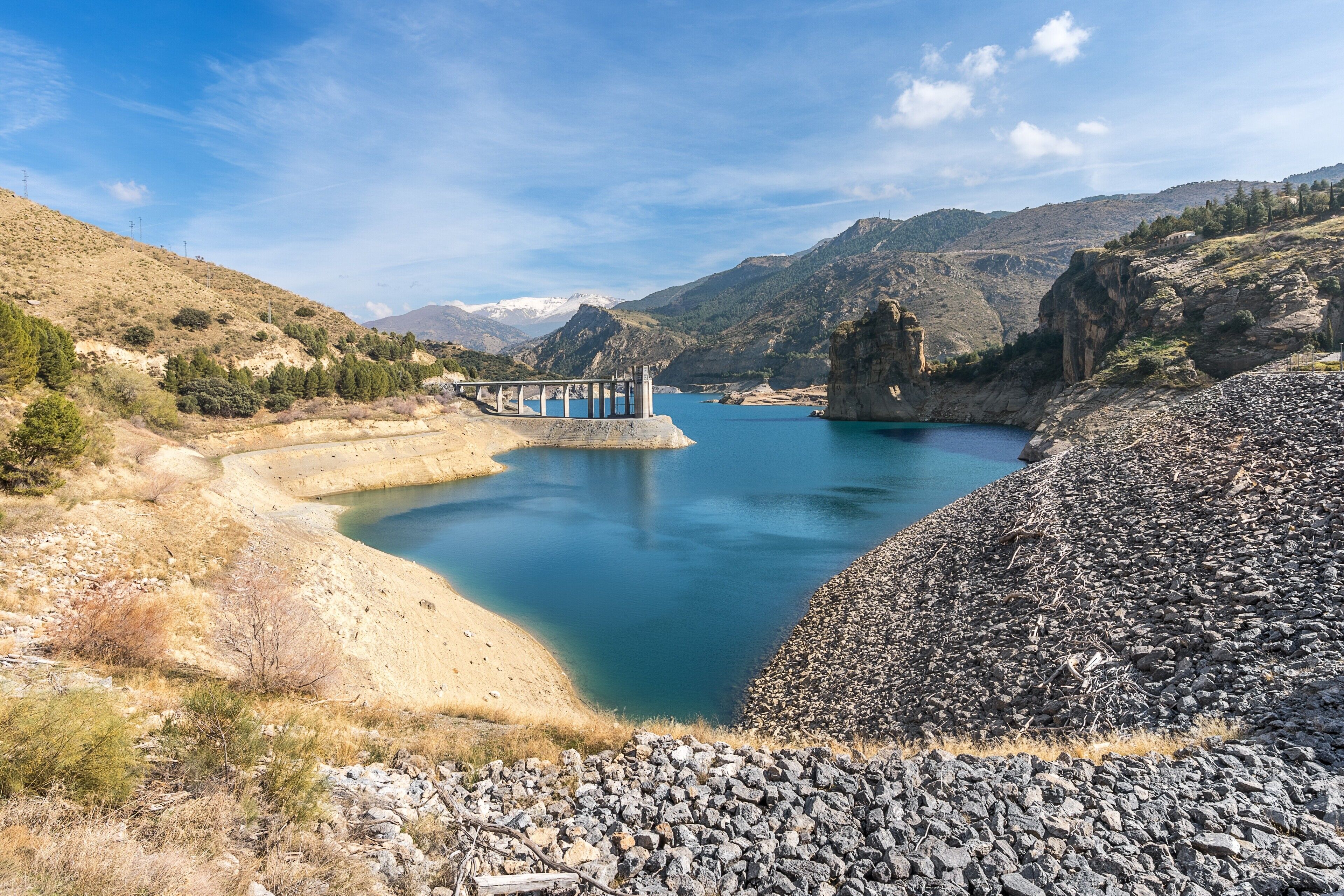 A reservoir with a dam, rocky terrain, and a bridge.