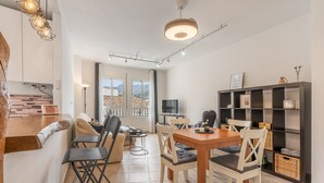Un espace de vie moderne comprenant une cuisine, un coin repas et un téléviseur. On y trouve plusieurs options d’assises ainsi qu’une bibliothèque.
