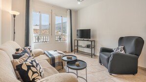 Un salon comprenant un canapé, un fauteuil, un meuble pour la télévision et deux petites tables.