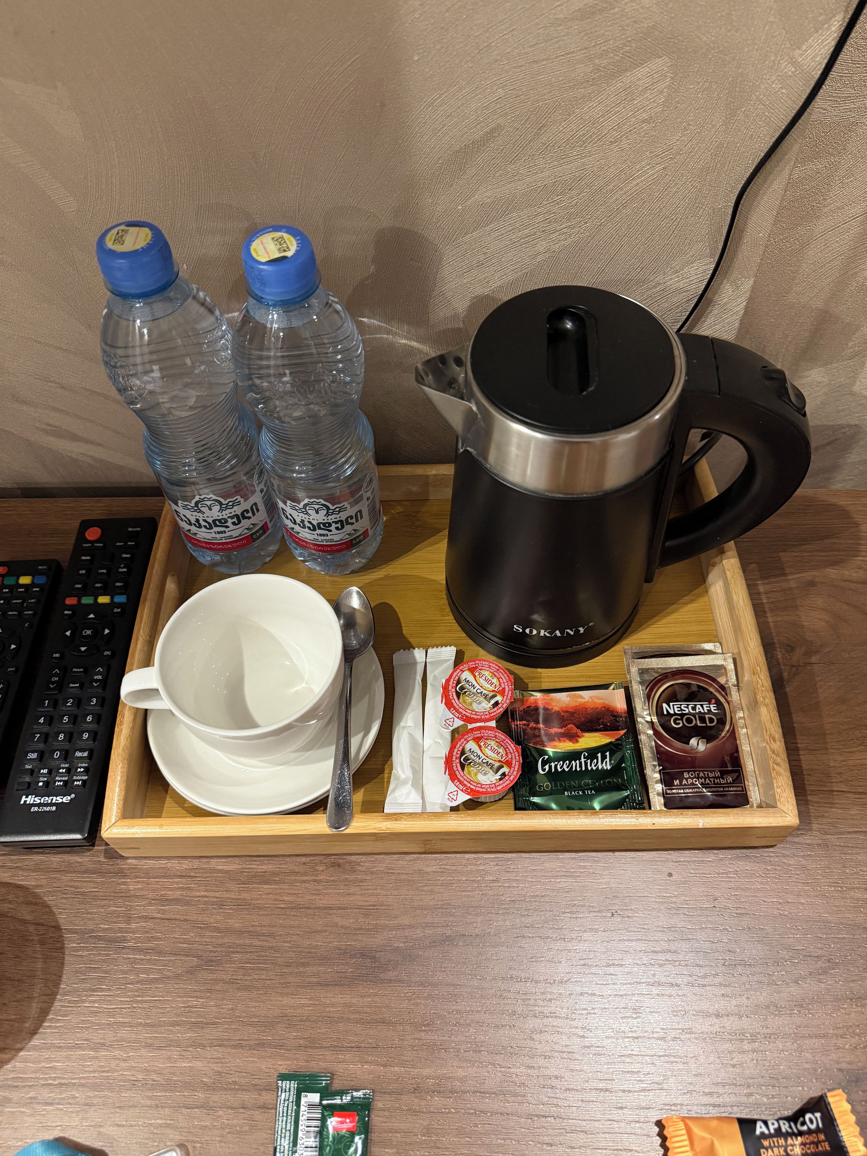 Una bandeja con cafetera, botellas de agua, una taza, una cuchara y porciones de comida.