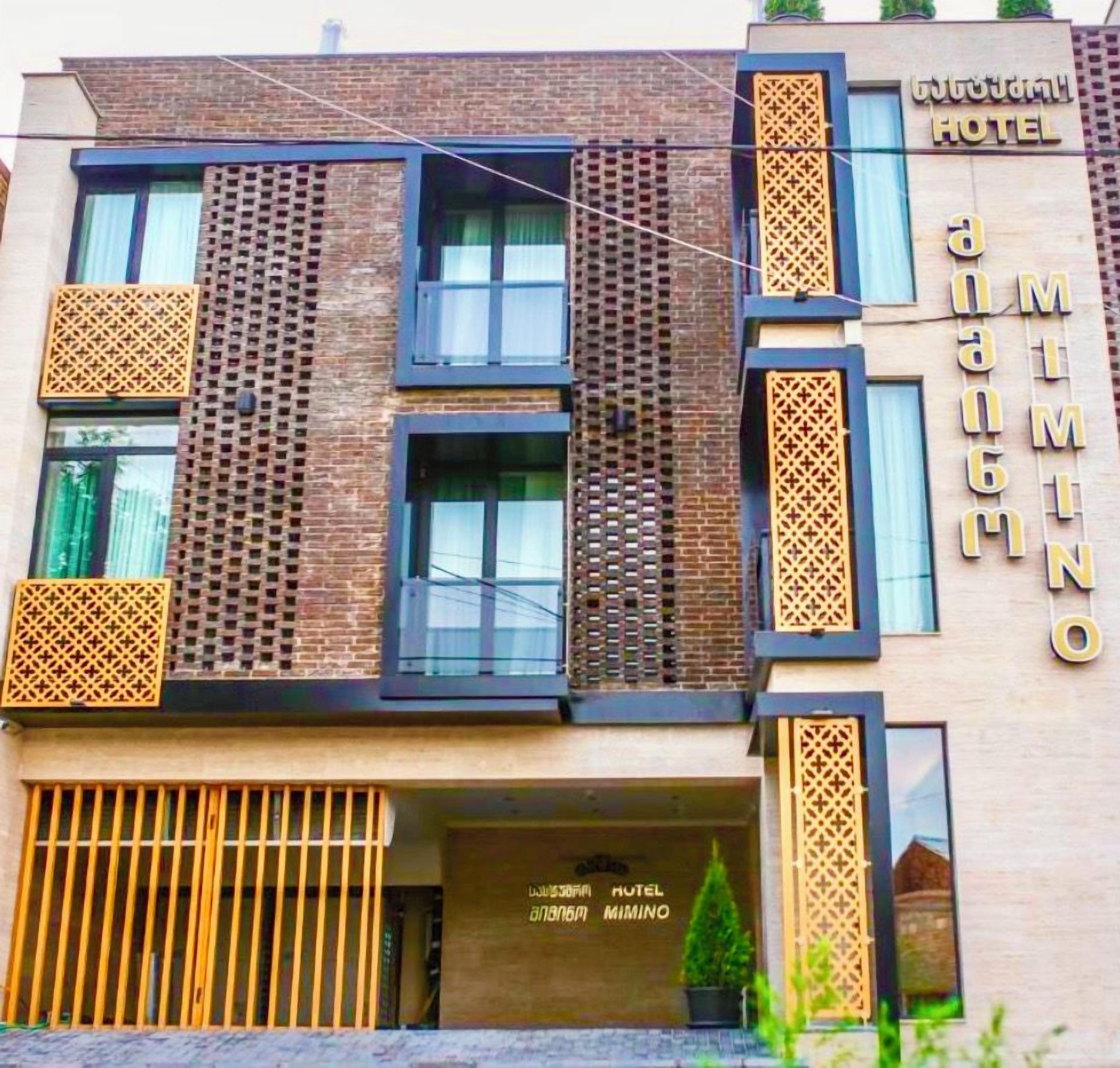 Fachada de hotel moderna con un cartel llamativo, ventanas amplias y paneles de madera ornamental.