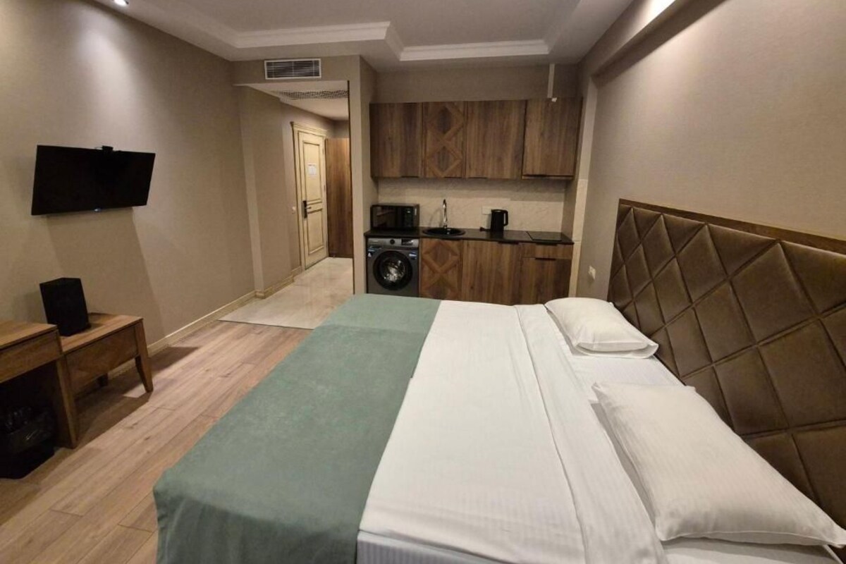 A hotel room with a bed, a television, a small table, and a kitchenette.